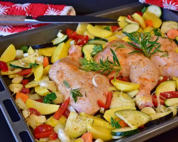 Sovracosce di pollo al forno con patate, zucchine, peperoni e rosmarino, pronte per essere infornate.