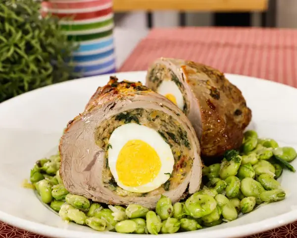 Fettina di carne ripiena con uovo sodo e spinaci, servita su un letto di fave.