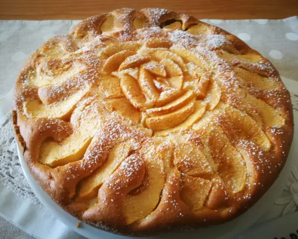 Deliziosa torta di mele senza glutine, con mele disposte a rosa al centro e spolverata di zucchero a velo.