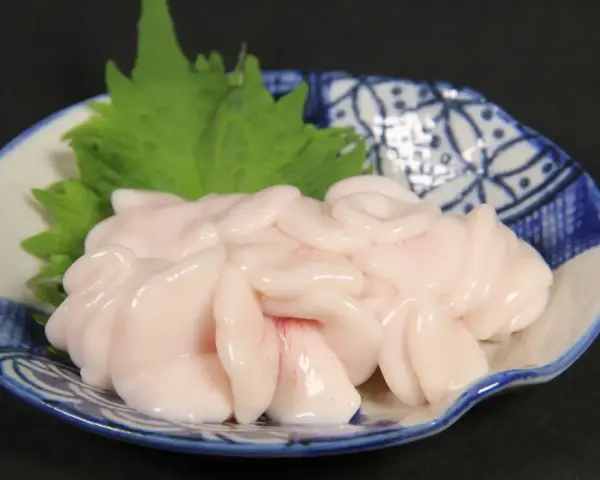 Piatto di lattume di tonno, delicato e rosato, guarnito con una foglia verde su un piatto decorato.