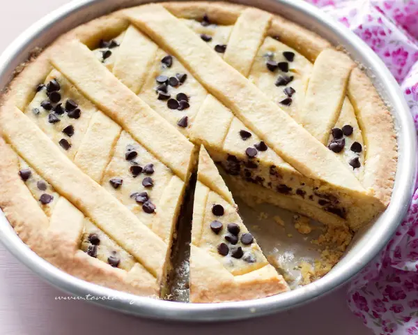 Una deliziosa crostata di ricotta con gocce di cioccolato, con una fetta tagliata per mostrare il ripieno cremoso.