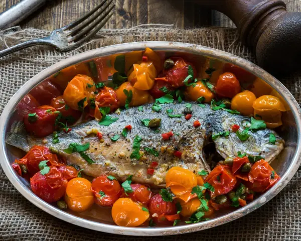 Orata all'acqua pazza, un piatto saporito con pomodorini, capperi e prezzemolo, pronto per essere gustato.