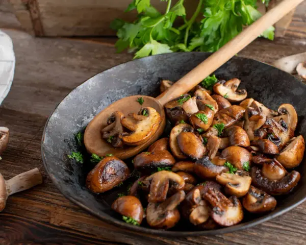 Funghi in padella dorati e saporiti, guarniti con prezzemolo fresco, pronti per essere gustati.