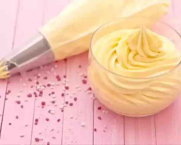 Sac à poche con crema al burro pronta per decorare, accanto a un bicchiere colmo della stessa soffice crema.