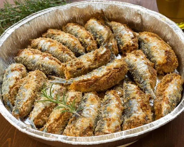 Sardine al forno dorate e croccanti, disposte in una teglia d'alluminio con rametti di rosmarino.