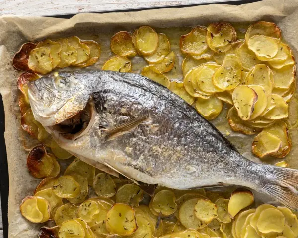 Orata al forno dorata e succulenta, adagiata su un letto di patate croccanti e aromatiche.