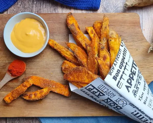Patate dolci al forno croccanti, servite in un cono di carta con una salsa cremosa e paprika.