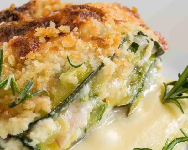 Una fetta di parmigiana di zucchine bianca senza besciamella, dorata e croccante, con rosmarino fresco.