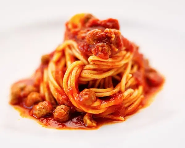 Un piatto di spaghetti alla teramana, conditi con un ricco sugo di pomodoro e polpettine, serviti su un piatto bianco.