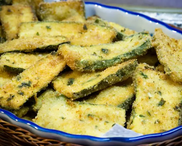 Fette di zucchine gratinate in padella, dorate e croccanti, servite in una ciotola blu bordata di bianco.