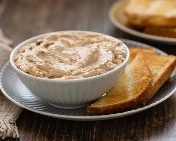 Una ciotola di cremosa mousse di tonno, servita con fette di pane tostato dorato. Perfetta per un aperitivo veloce.