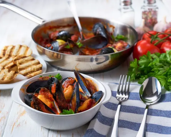 Cozze alla tarantina fumanti in una ciotola bianca, accompagnate da pane grigliato e ingredienti freschi.