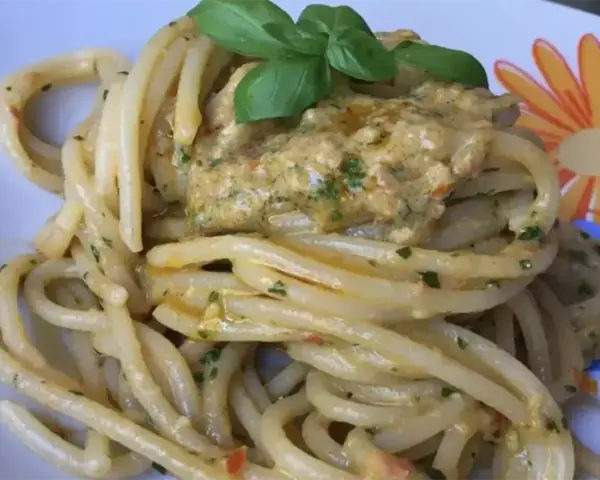 Un piatto invitante di pasta alla carlofortina, condita con un sugo cremoso e guarnita con basilico fresco.