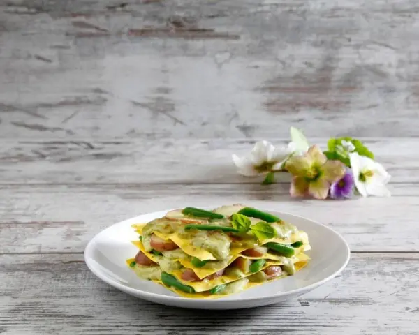 Lasagne al pesto con fagiolini e patate, un piatto colorato e gustoso su un tavolo di legno.