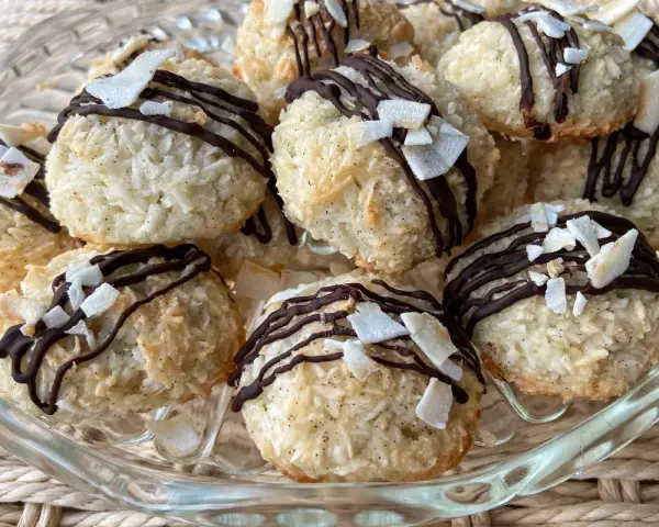Deliziosi dolcetti al cocco, ricoperti da cioccolato fondente e scaglie di cocco croccante, su un piatto di vetro.
