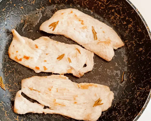 Tre fette di tacchino in padella, morbido e profumato al rosmarino, pronte per essere gustate.