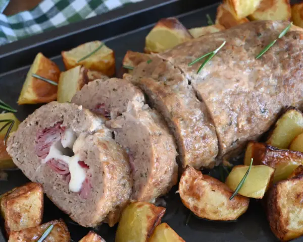 Polpettone al forno ripieno di prosciutto e formaggio filante, servito con patate arrosto e rosmarino.