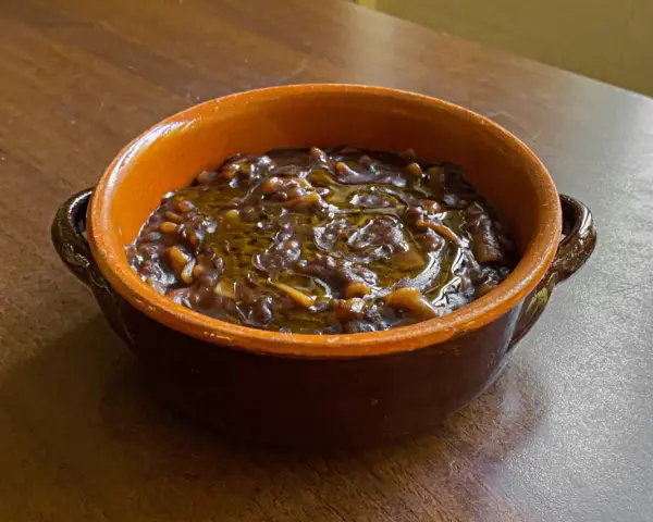 Un gustoso piatto di pasta e lenticchie, condito con olio d'oliva, servito in una ciotola di terracotta su un tavolo di legno.