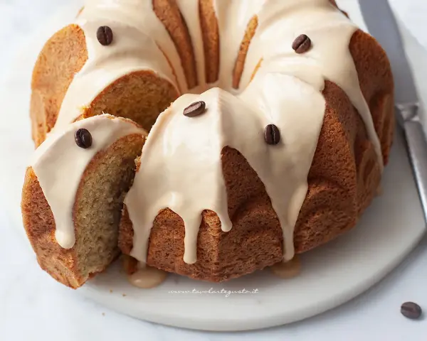 Torta al caffè soffice e profumata, ricoperta da una glassa chiara e decorata con chicchi di caffè. Una fetta è stata tagliata, rivelando l'interno morbido.