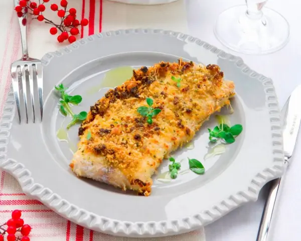 Delizioso merluzzo impanato al forno, dorato e croccante, guarnito con erbe fresche e servito su un piatto grigio.