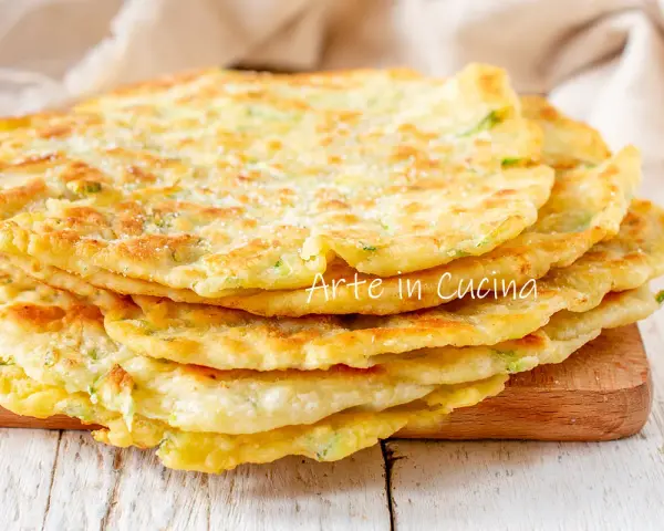 Una pila di schiacciate di zucchine dorate e soffici, cosparse di parmigiano, pronte per essere gustate.
