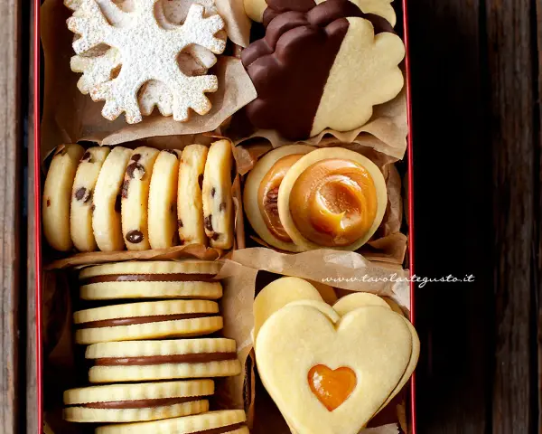 Scatola piena di biscotti al burro: a fiocco di neve, al cioccolato, con ripieno di caramello e a forma di cuore.