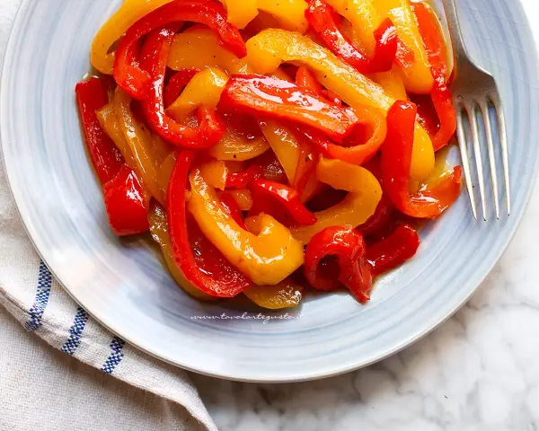 Piatto di peperoni in agrodolce, rossi e gialli, conditi con olio e spezie, pronti per essere gustati.