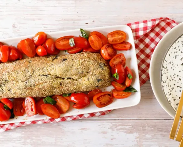 Polpettone di melanzane dorato e croccante, circondato da pomodorini freschi e basilico, pronto per essere gustato.