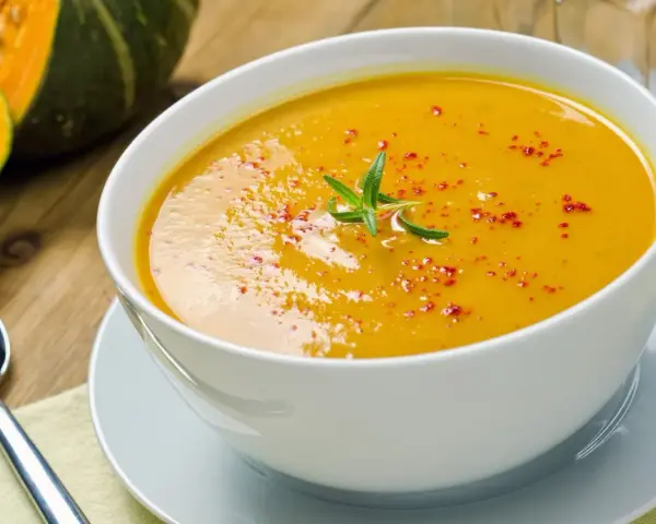 Una cremosa vellutata di zucca, guarnita con rosmarino e paprika, pronta per essere gustata.