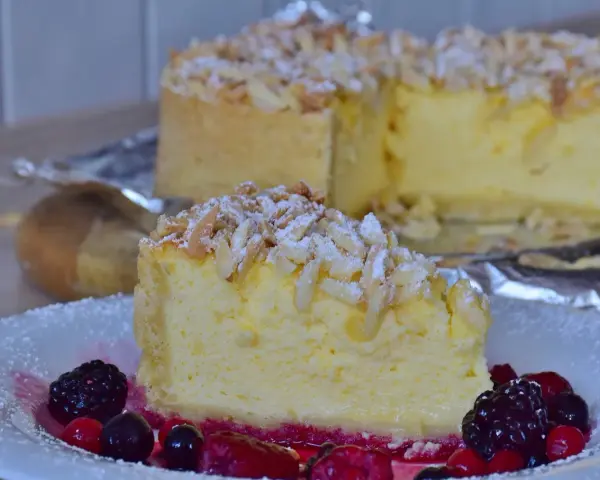 Una fetta di torta di riso cremosa, guarnita con mandorle a lamelle e frutti di bosco, su un piatto bianco.