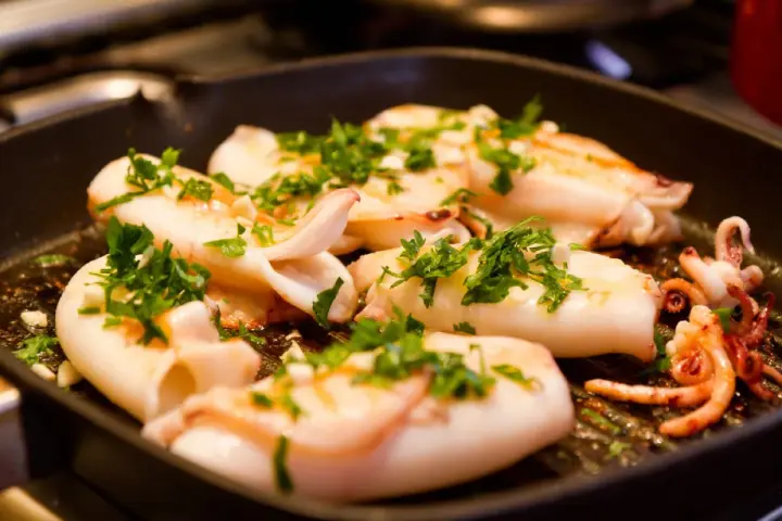Seppie alla griglia succulente, cosparse di prezzemolo fresco, cuociono in una padella scanalata, pronte per essere gustate.