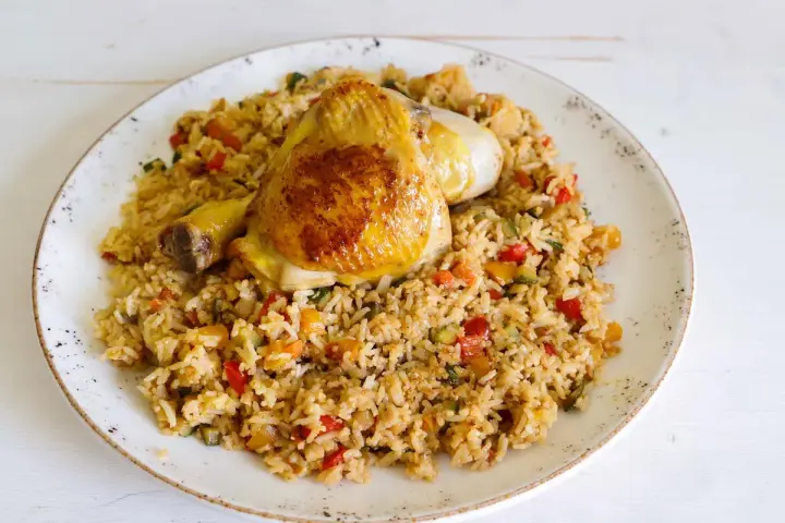 Fusi di pollo in padella serviti su un letto di riso saltato con verdure colorate.