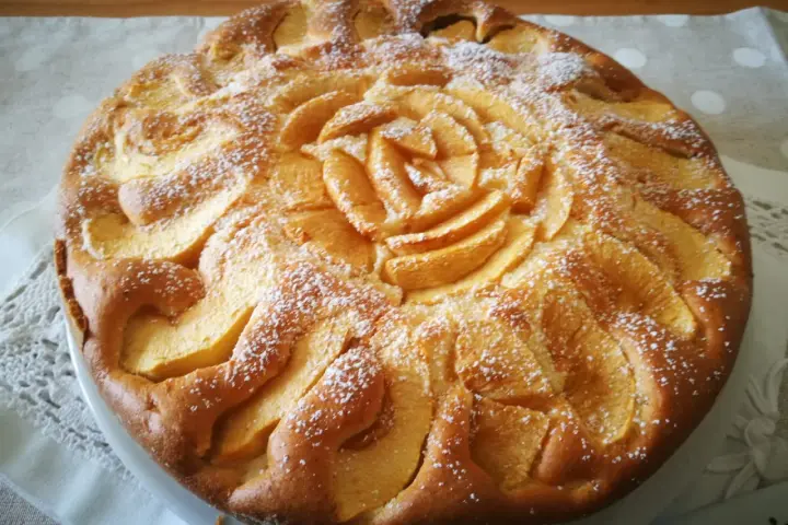 Deliziosa torta di mele senza glutine, con mele disposte a rosa al centro e spolverata di zucchero a velo.