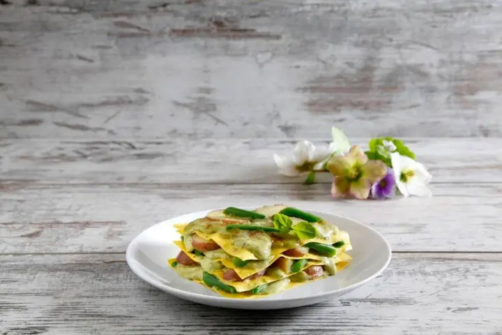 Lasagne al pesto con fagiolini e patate, un piatto colorato e gustoso su un tavolo di legno.