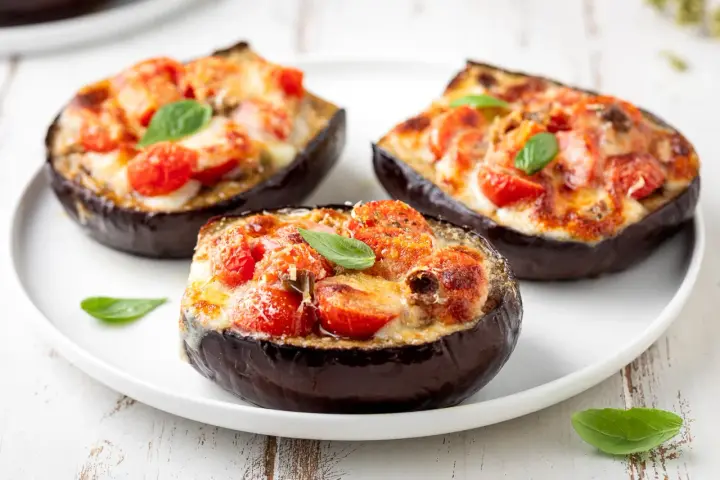 Melanzane ripiene al forno velocissime, con pomodorini, formaggio filante e basilico fresco. Un piatto invitante e facile da preparare.