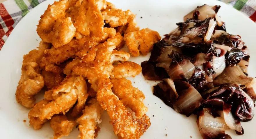 Straccetti di pollo al forno dorati e croccanti, serviti con radicchio stufato. Un piatto semplice e gustoso.