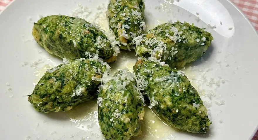 Strangolapreti alla trentina, verdi e saporiti, spolverati di formaggio grattugiato su un piatto bianco.