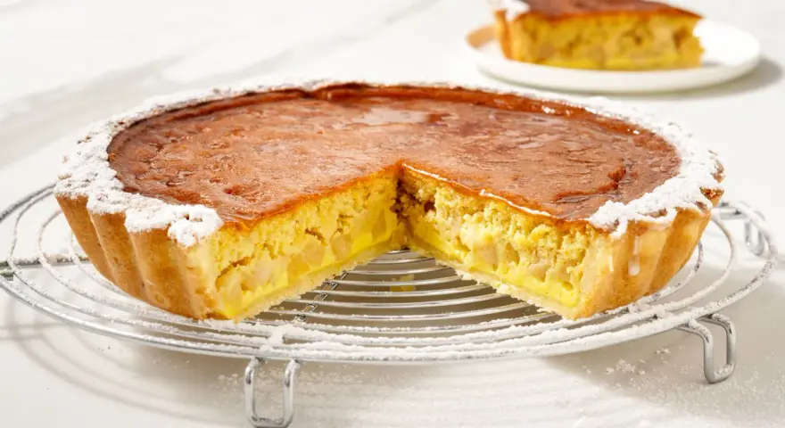Una fetta di torta di mele con crema pasticcera, cosparsa di zucchero a velo, su una griglia.