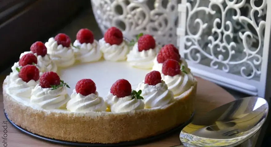 Cheesecake senza gelatina decorata con panna montata e lamponi freschi, pronta per essere servita.