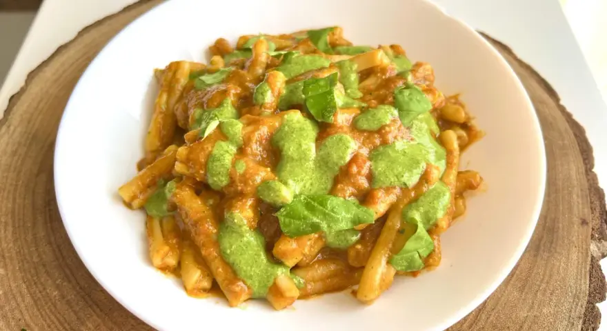 Un piatto di pasta alla Portofino, con un sugo rosso e un pesto verde brillante, guarnito con foglie di basilico fresco.