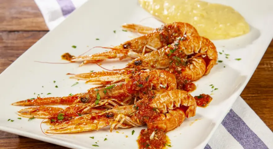 Scampi alla busara succulenti su piatto bianco, con un contorno di polenta gialla.