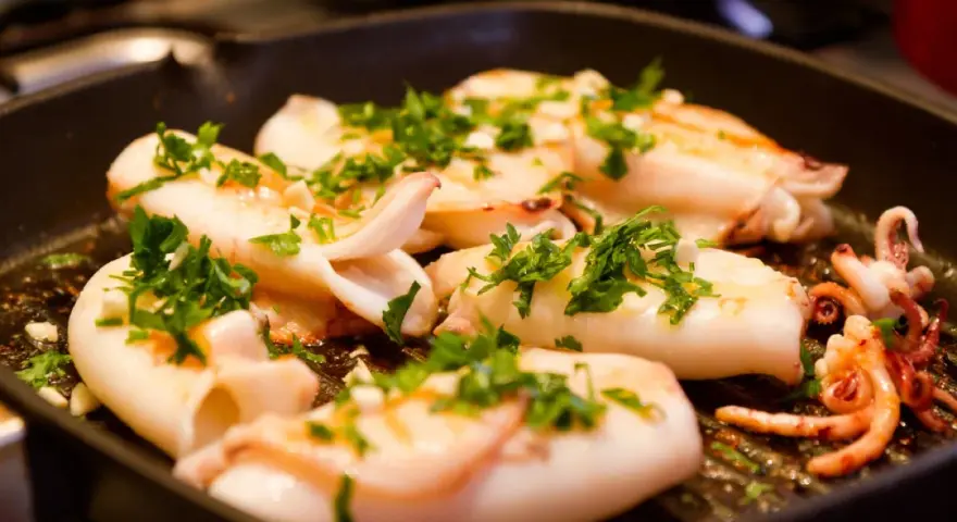 Seppie alla griglia succulente, cosparse di prezzemolo fresco, cuociono in una padella scanalata, pronte per essere gustate.