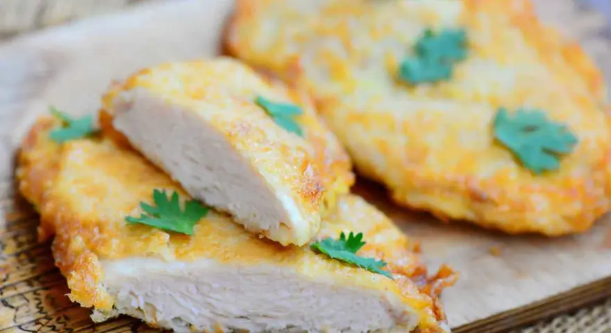 Deliziose cotolette di pollo dorate, tagliate a metà per mostrare la succosa carne bianca, guarnite con prezzemolo fresco.
