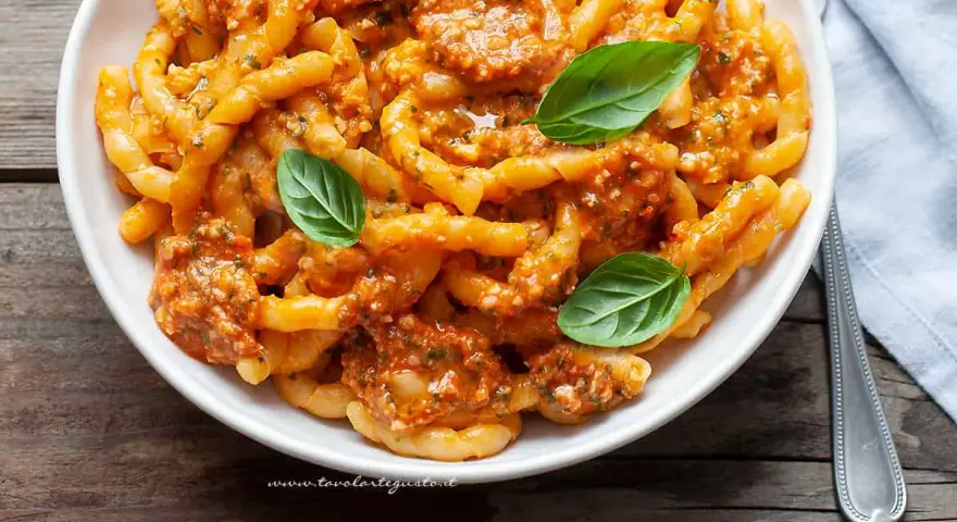 Busiate alla trapanese, un piatto di pasta siciliana con un ricco sugo rosso, guarnito con basilico fresco.