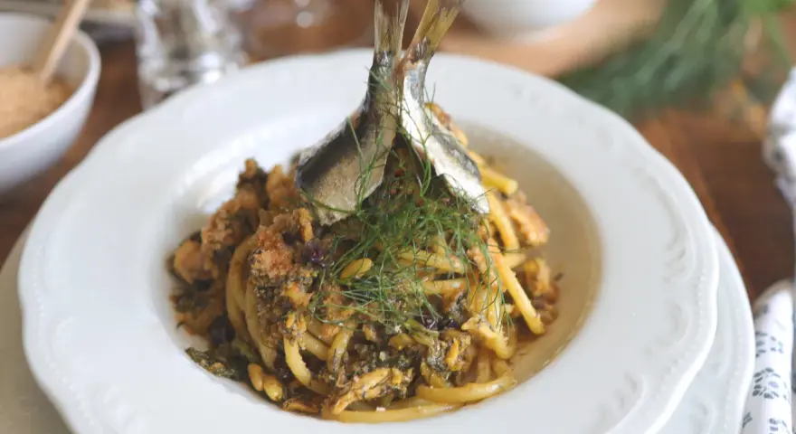 Un piatto di pasta con le sarde, guarnito con finocchietto fresco e due pesciolini interi. Un classico siciliano pronto da gustare.