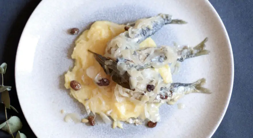 Sarde in saor su un letto di polenta, con cipolle caramellate e uvetta. Un classico veneto.
