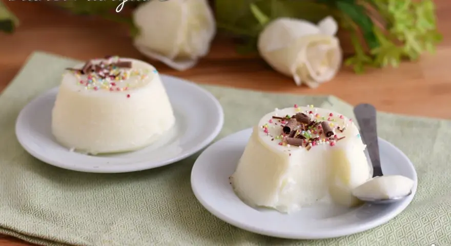 Biancomangiare ricetta originale siciliana: due dolci al cucchiaio bianchi, guarniti con codette colorate e scaglie di cioccolato, su piattini bianchi.