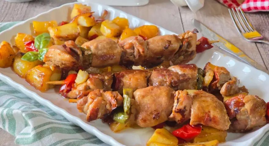 Spiedini di carne succulenti con patate arrosto e peperoni colorati, un piatto invitante e saporito.