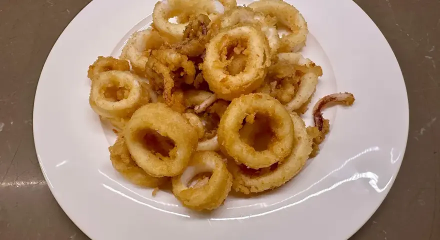 Un piatto bianco pieno di frittura di calamari dorata e croccante, un antipasto invitante.