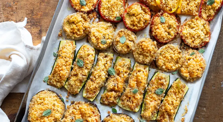 Verdure gratinate al forno: zucchine, melanzane, pomodori e peperoni ripieni di pangrattato e erbe aromatiche, cotti su una teglia.